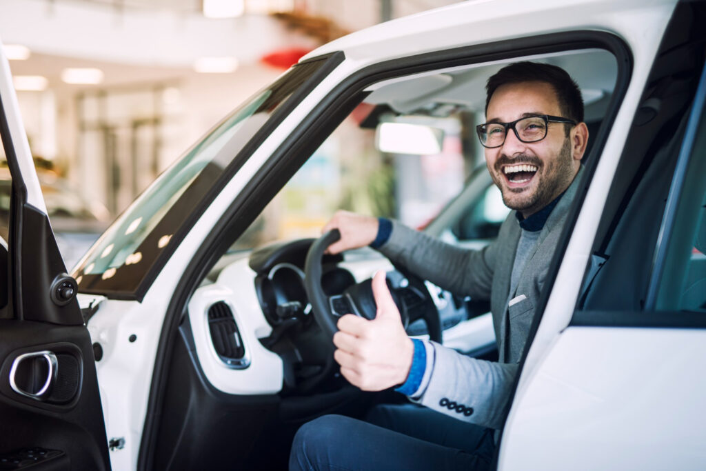 Hombre feliz con pulgar arriba dentro de vehículos usados